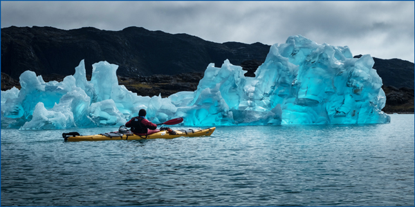 <span>Challenging Outdoor Sports:</span> A watchful kayaker paddles through a glacial lagoon, navigating past an outcropping of small icebergs.