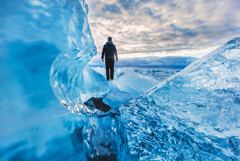 A man walks through icebergs on Diamond Beach, Iceland.