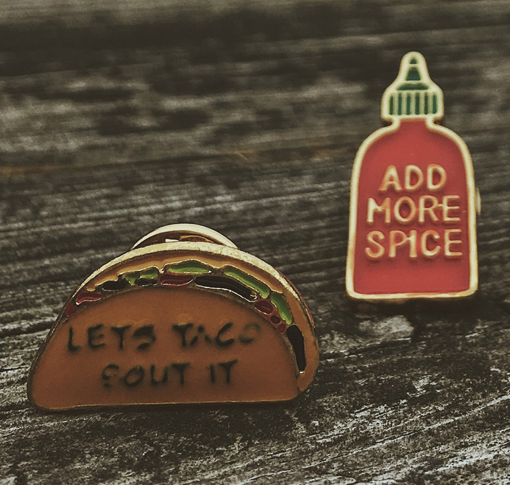 taco and hot sauce costume jewelry pins on distressed wood background